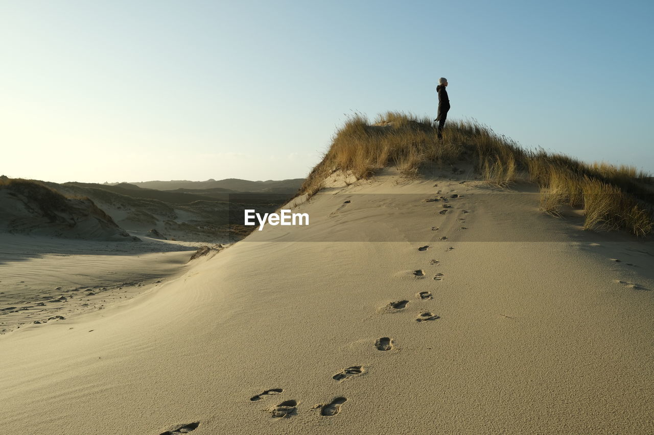 MAN STANDING ON BEACH AGAINST SKY