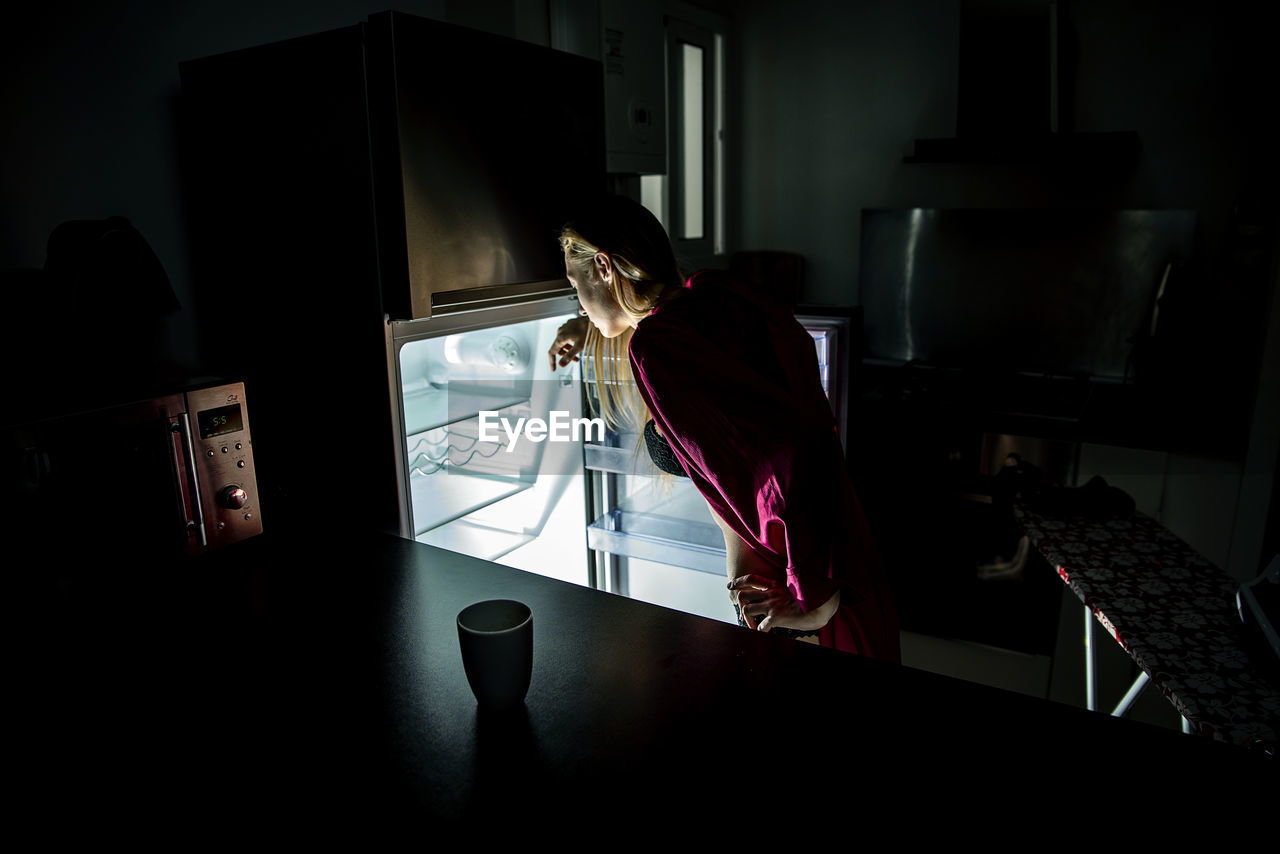 Rear view of woman looking into refrigerator at home
