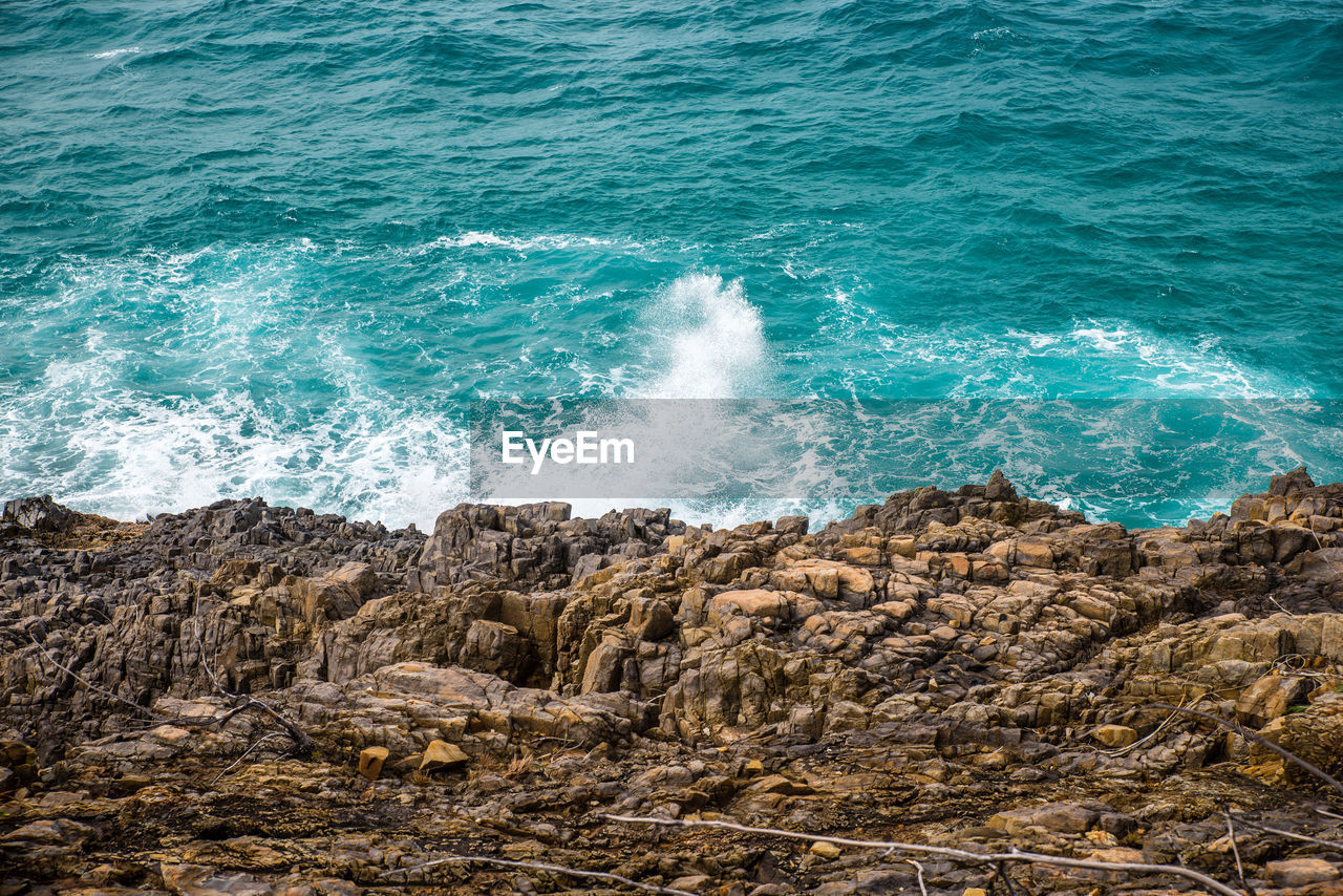 High angle view of waves splashing on rock in sea