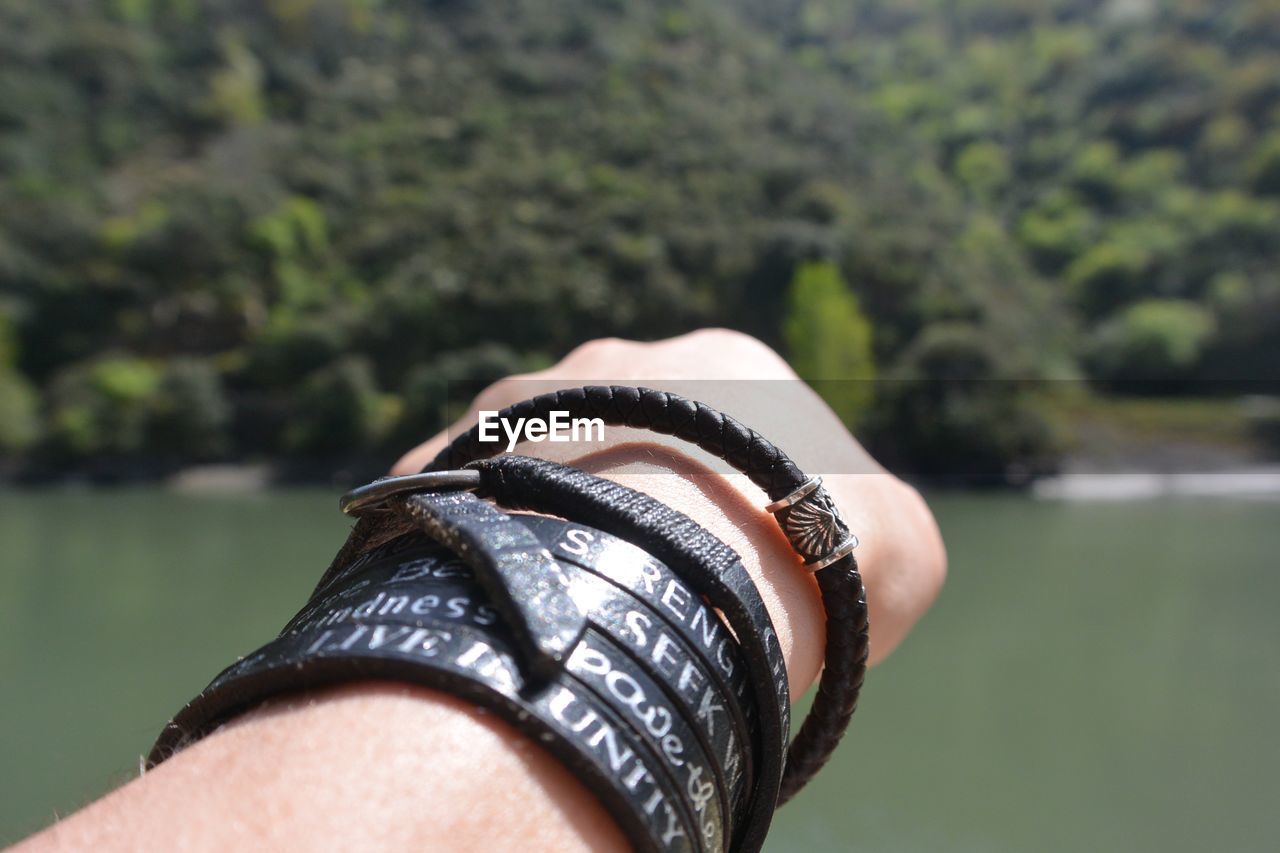 Cropped hand with black bracelets against river on sunny day