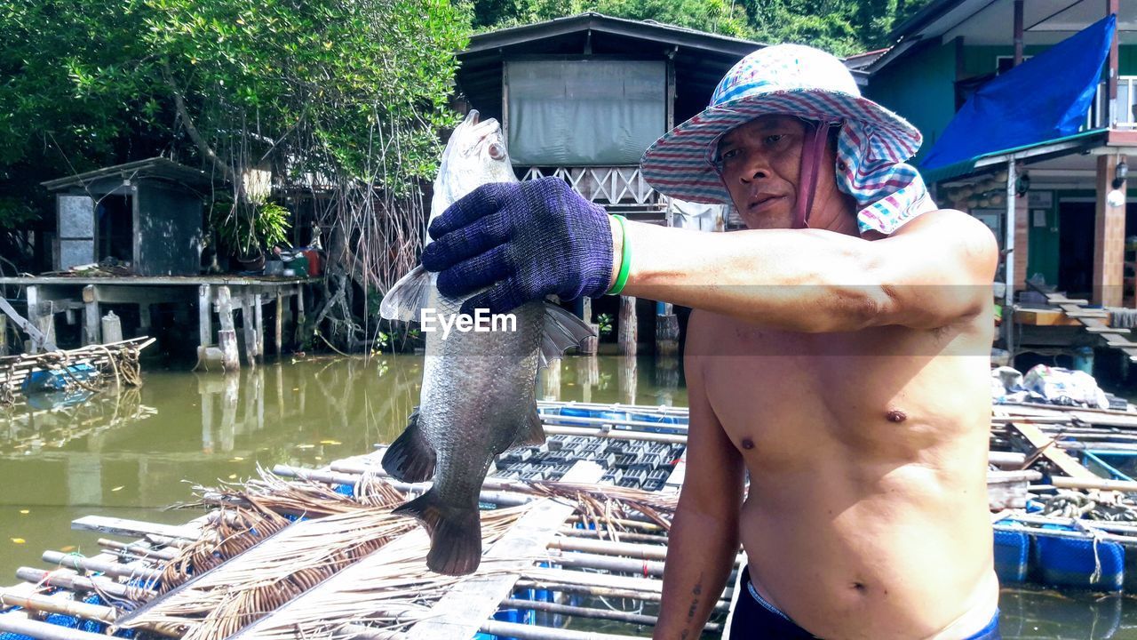 Shirtless fisherman looking at dead fish in river