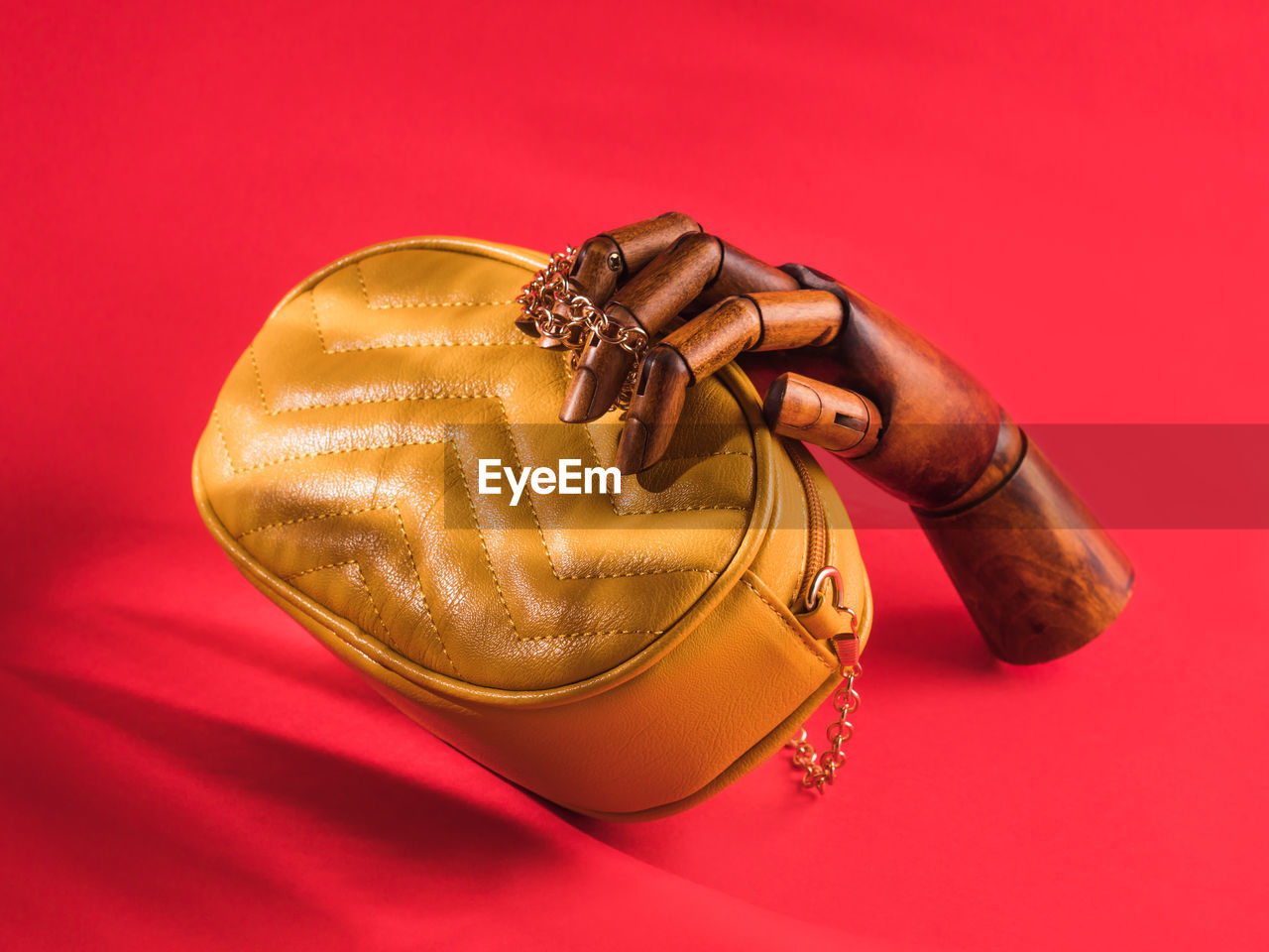Wooden hand holding yellow eco leather bag on red background. female fashion accessories