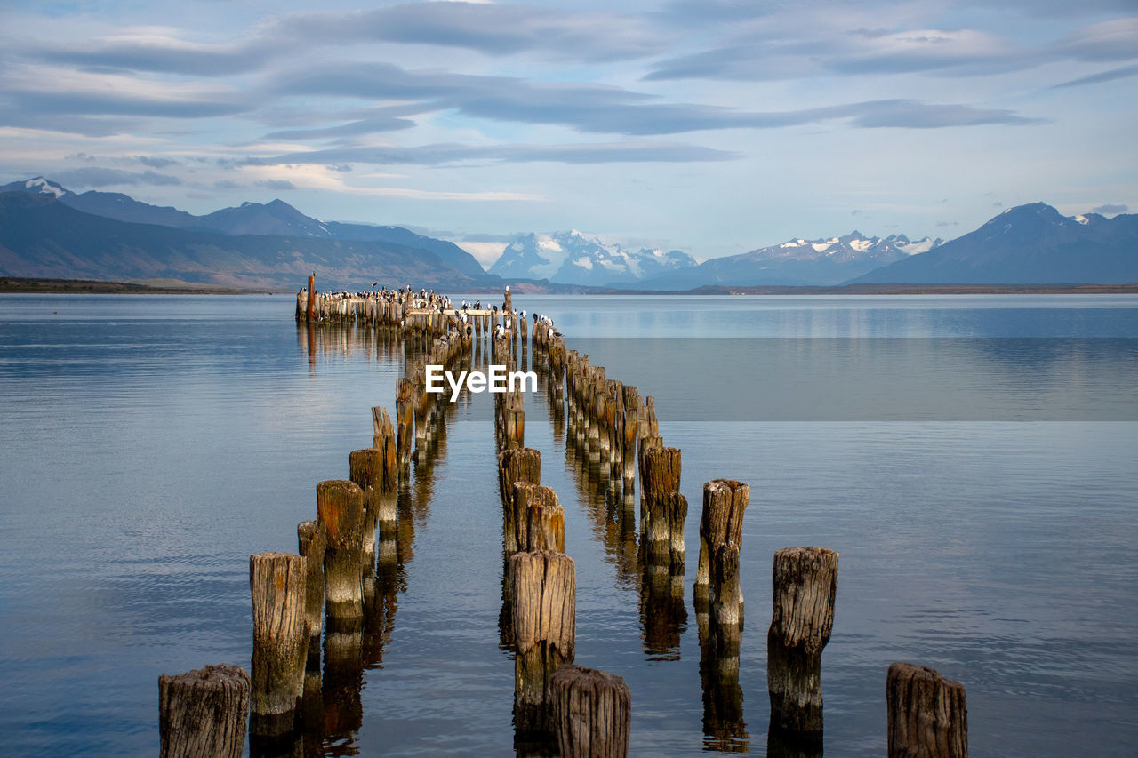 Wooden posts in lake against sky