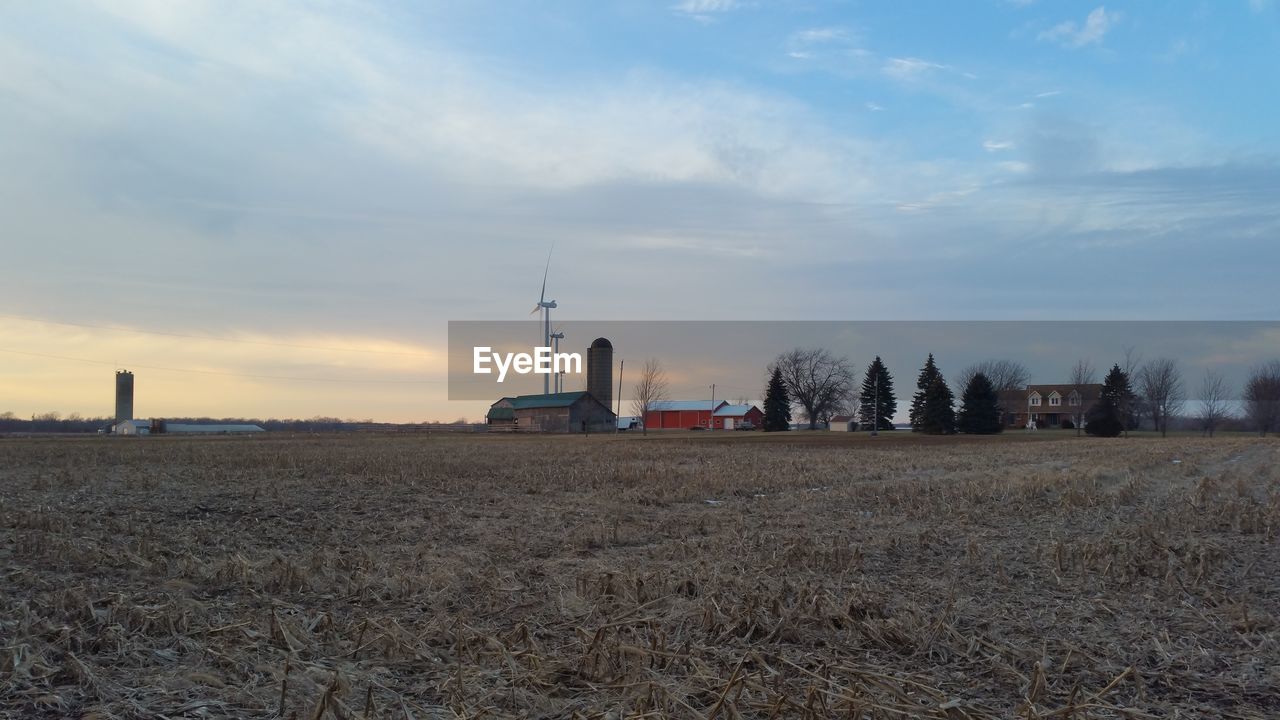 Barn and wind turbines on field against sky