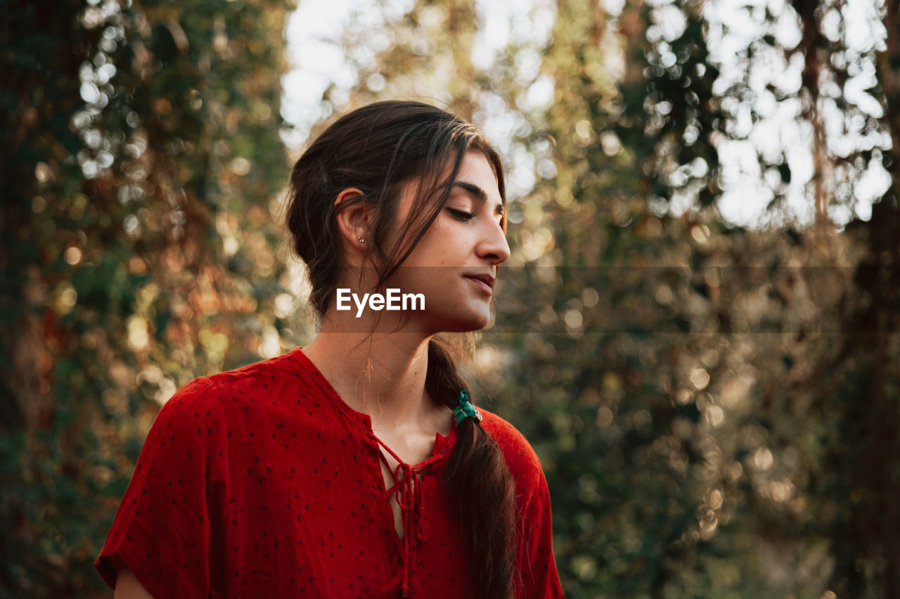 Close-up of woman looking away while standing against trees