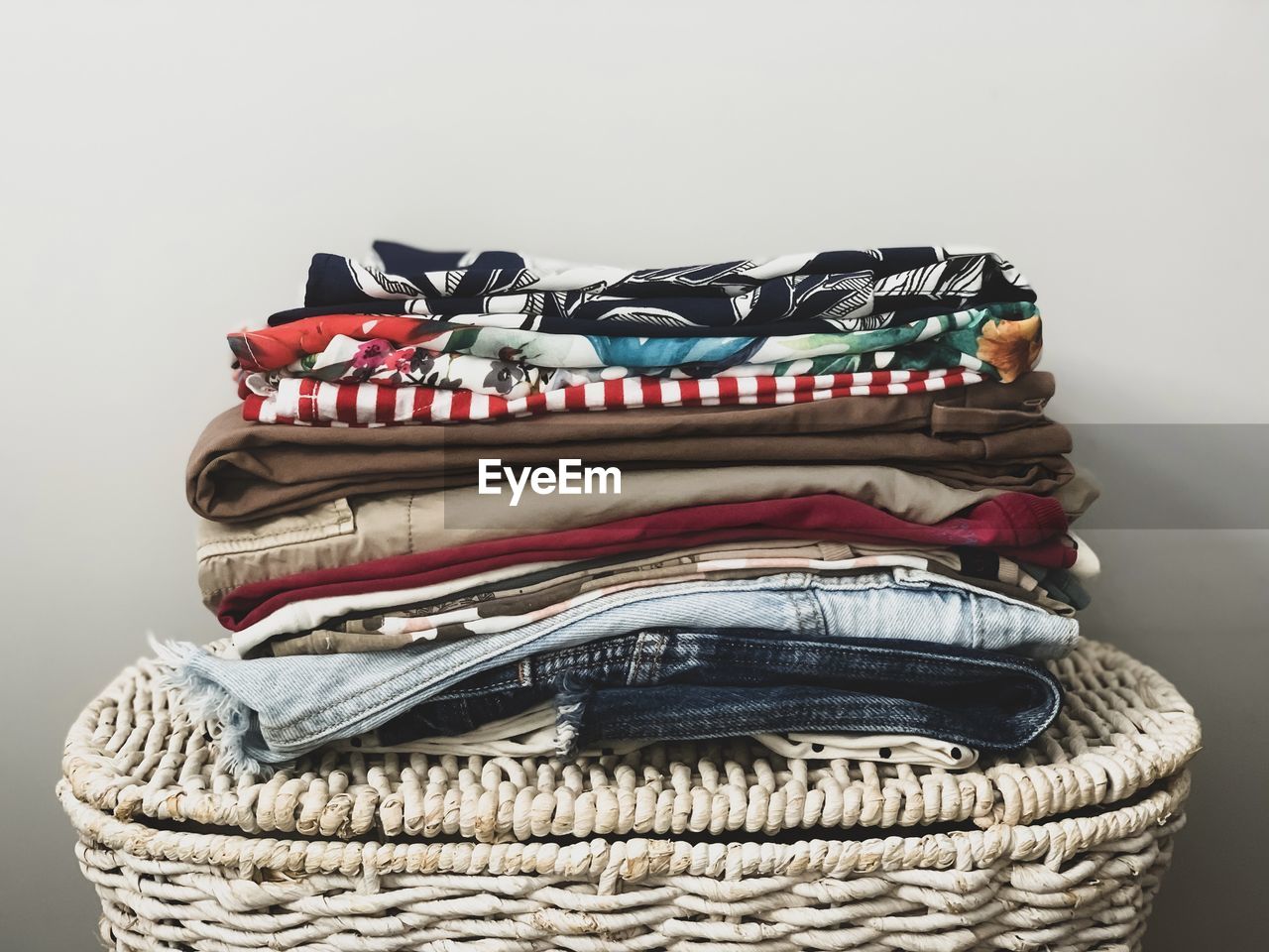 A pile of ironed colorful female clothes on a white wicker basket ready to be organised in wardrobe