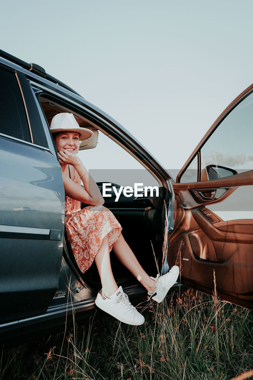 WOMAN SITTING IN CAR AGAINST SKY