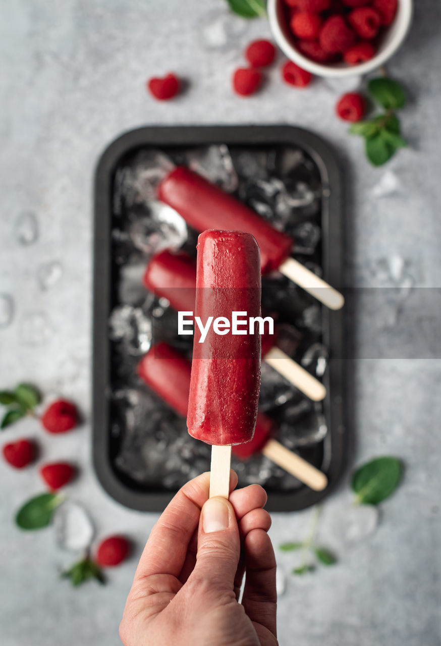 Hand holding raspberry popsicle above a tray of frozen treats.