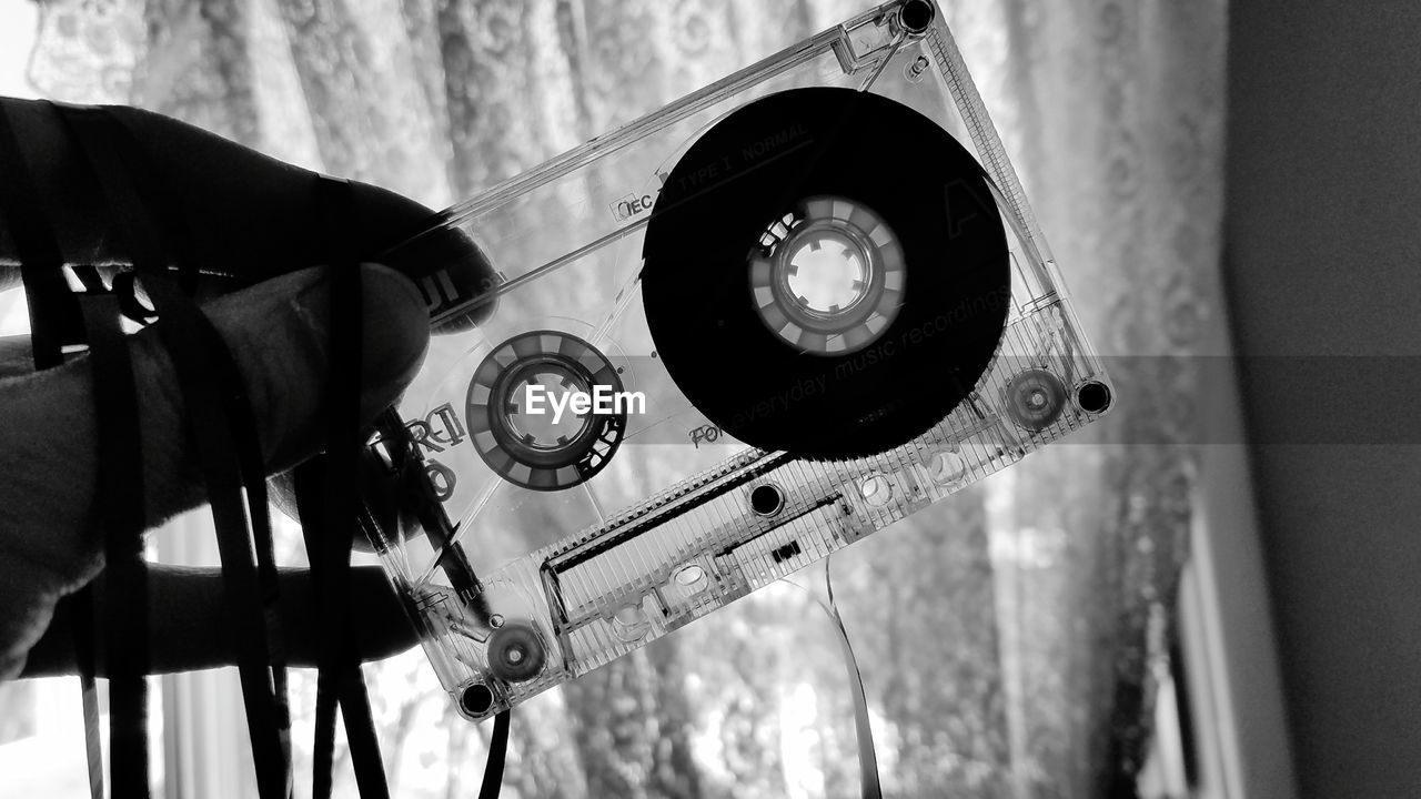 Cropped hand holding audio cassette by curtain at home