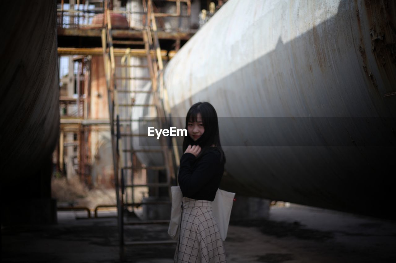 Portrait of young woman standing by pipe at industry