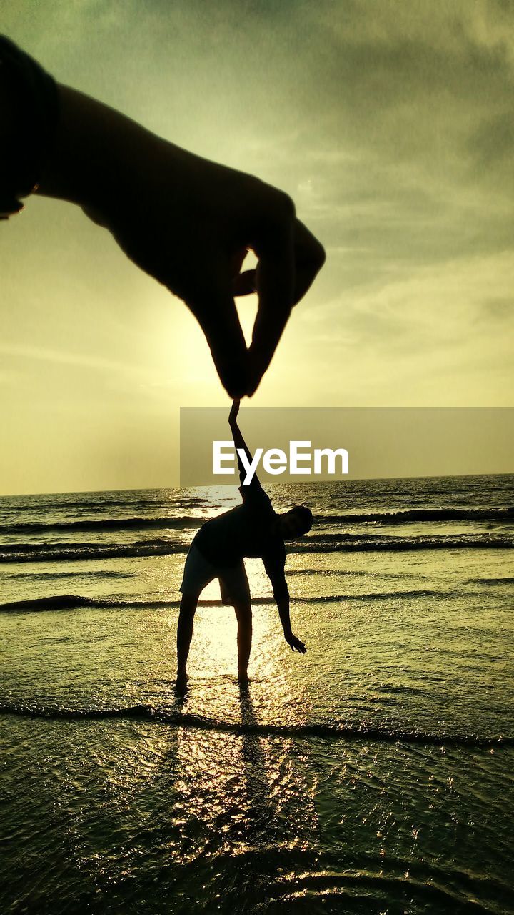 Optical illusion of cropped hand holding man hand at beach