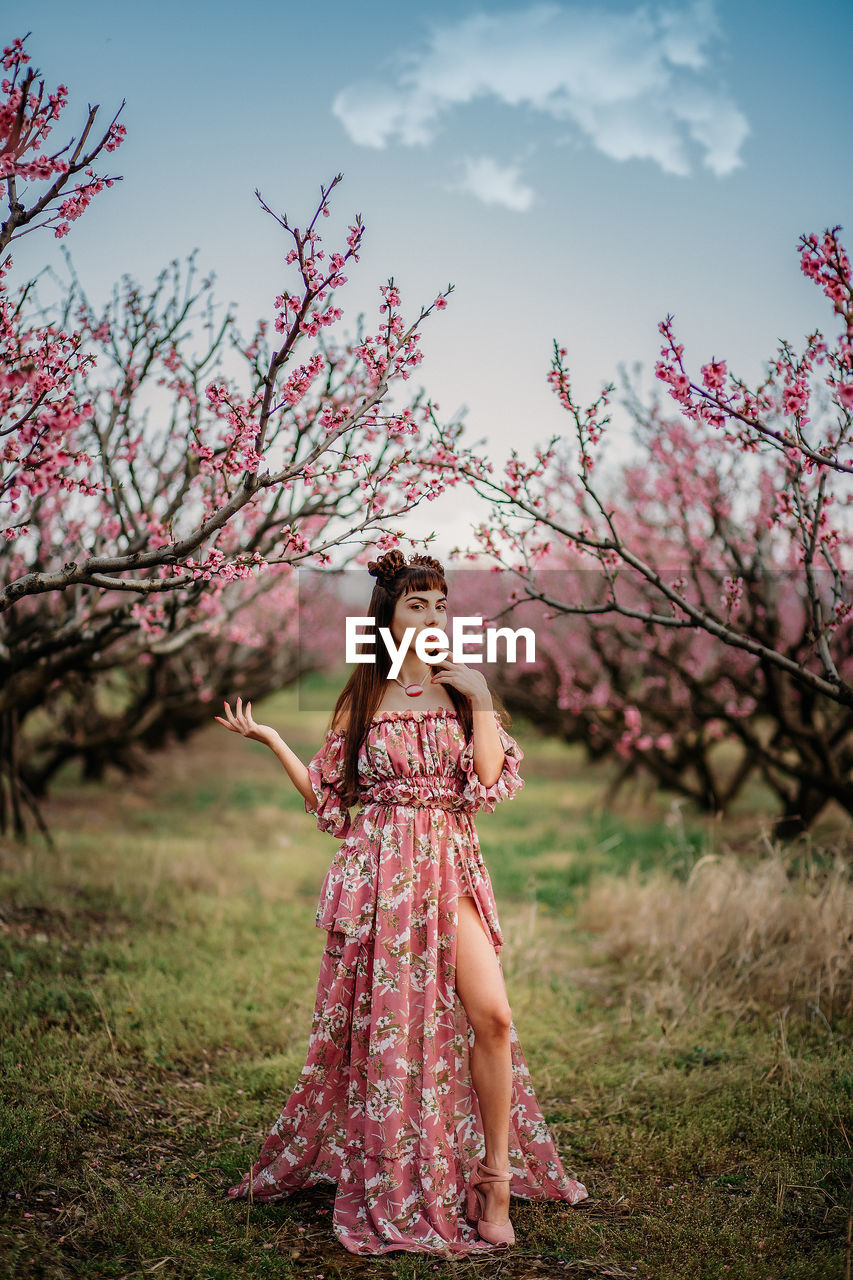 FULL LENGTH OF WOMAN STANDING BY PINK FLOWERING TREE