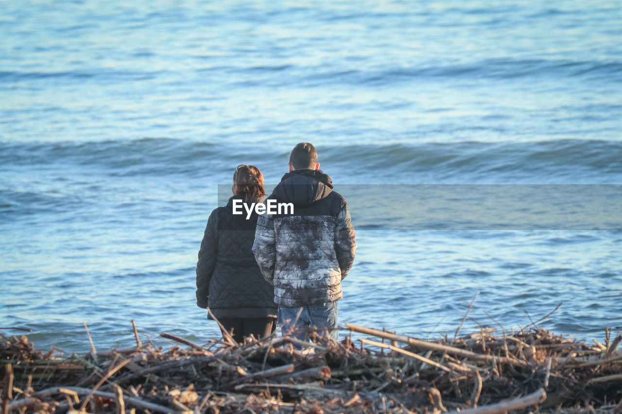REAR VIEW OF MAN AND WOMAN STANDING ON BEACH