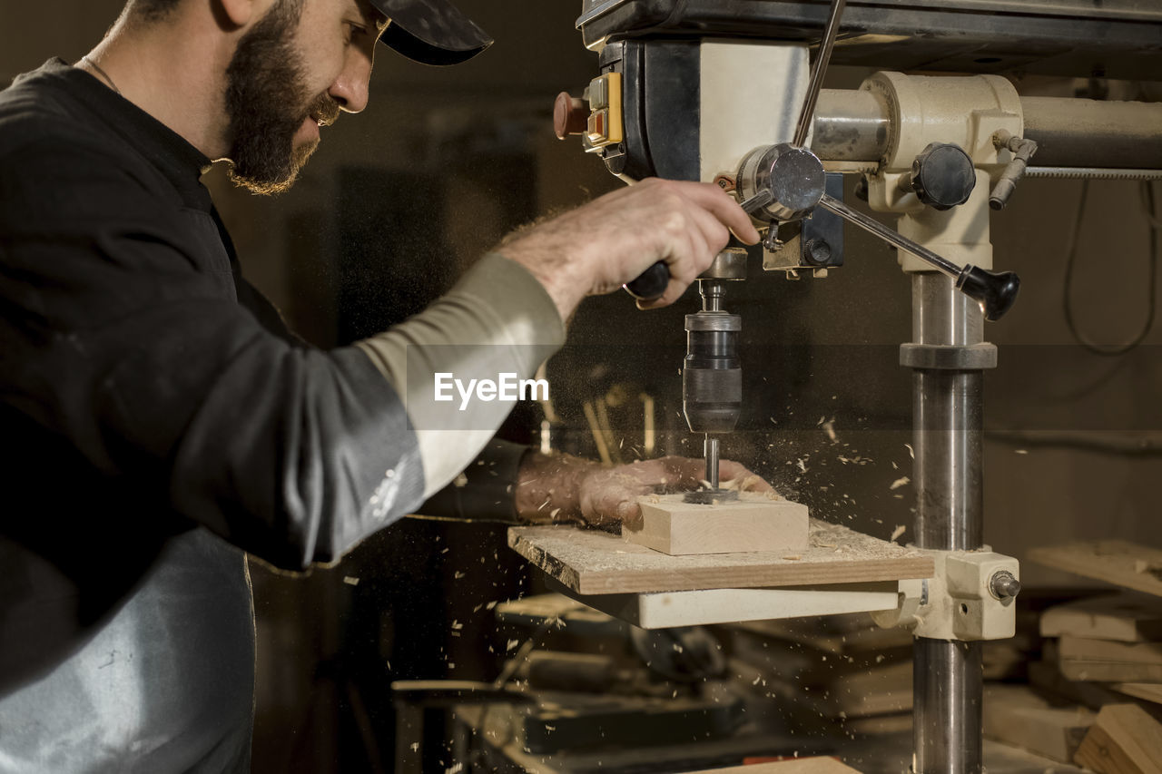 Craftsperson drilling wood with machine at workshop