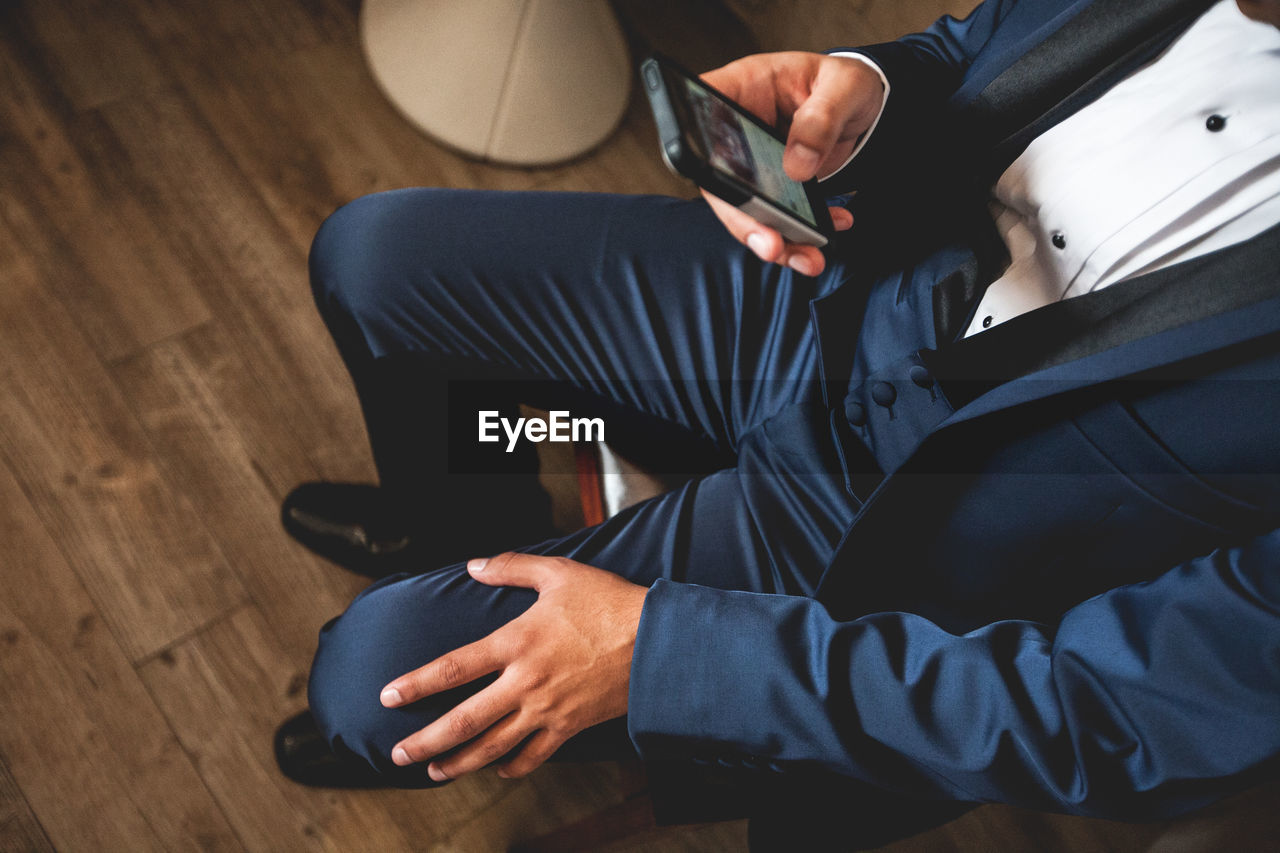 Low section of groom using phone while sitting on chair at home