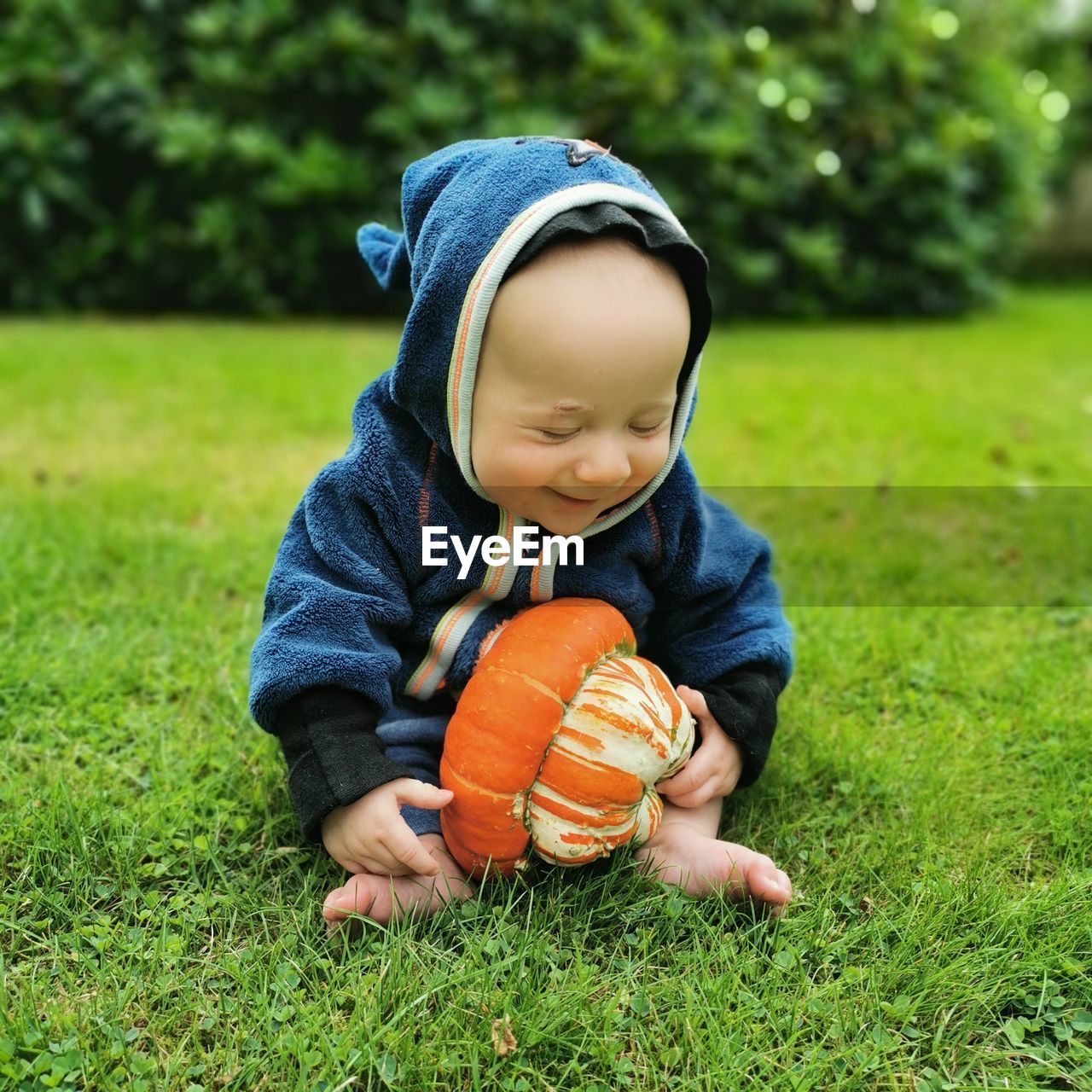 Close-up of cute baby boy playing with a pumpkin on a grassy field