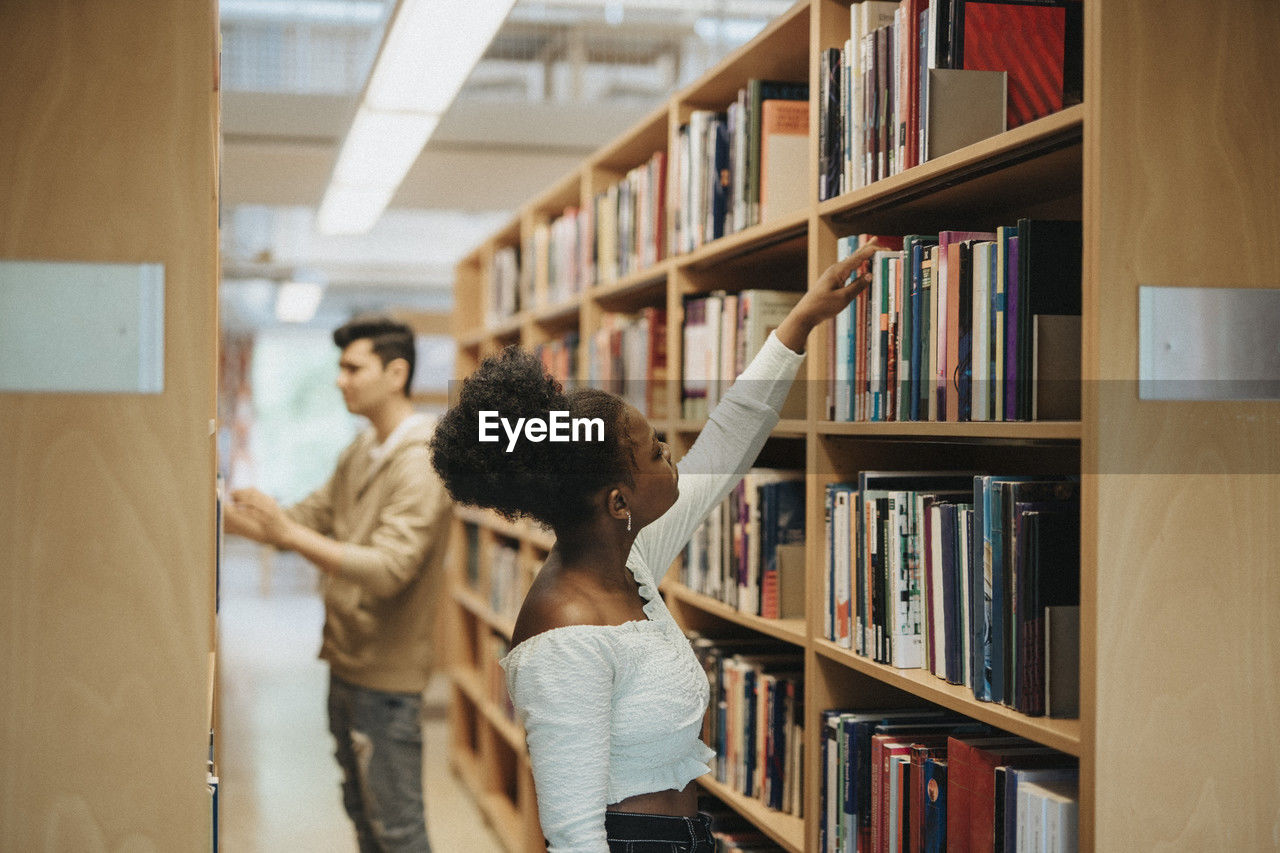 Side view of student searching books on bookshelf in library at university