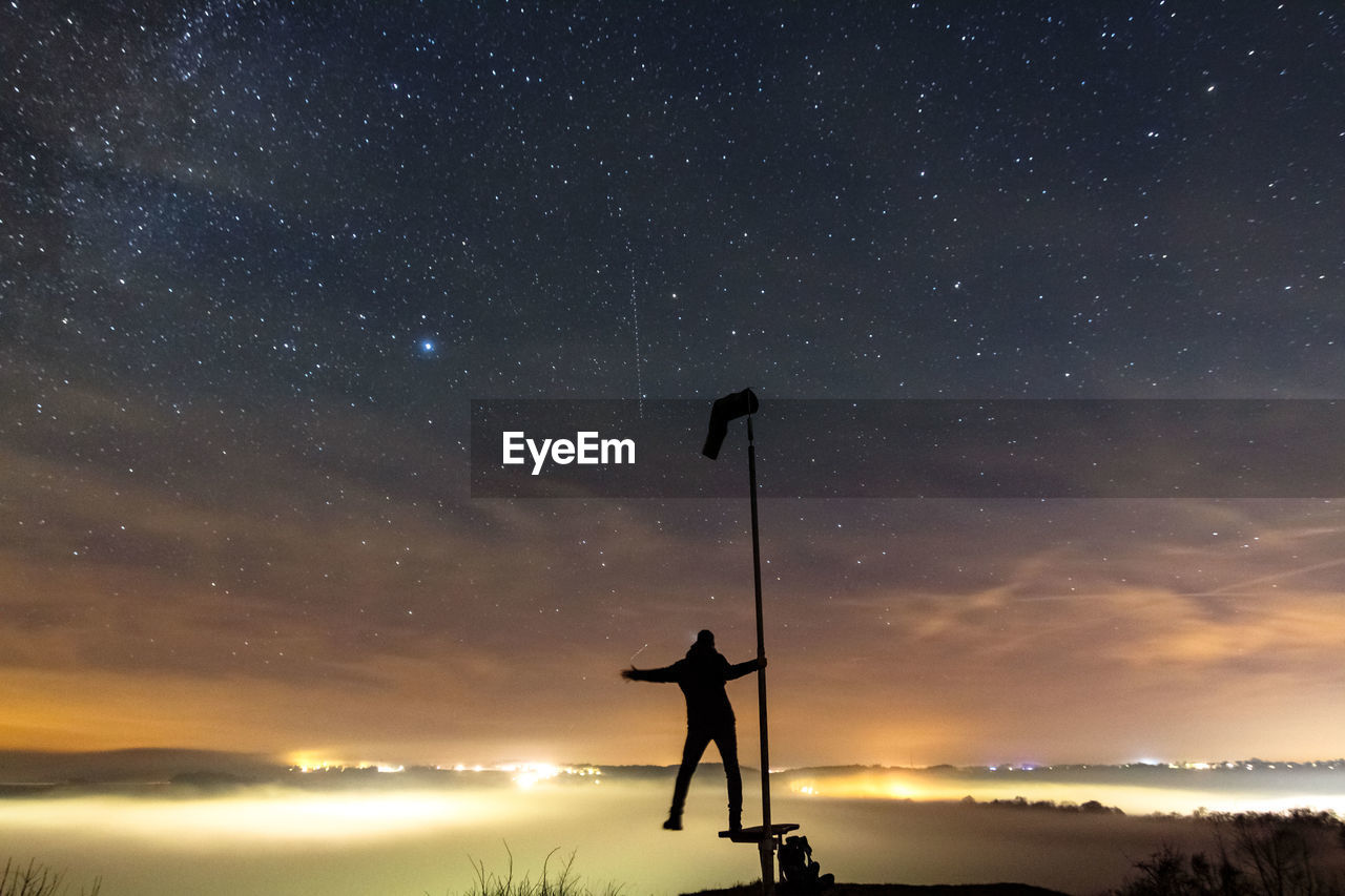 Silhouette man standing on pole against sky at night