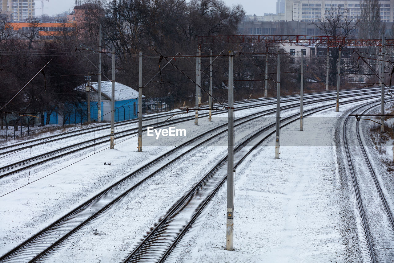 Snow-covered railroad tracks in a turn and a blue gatehouse in a thicket of bushes.