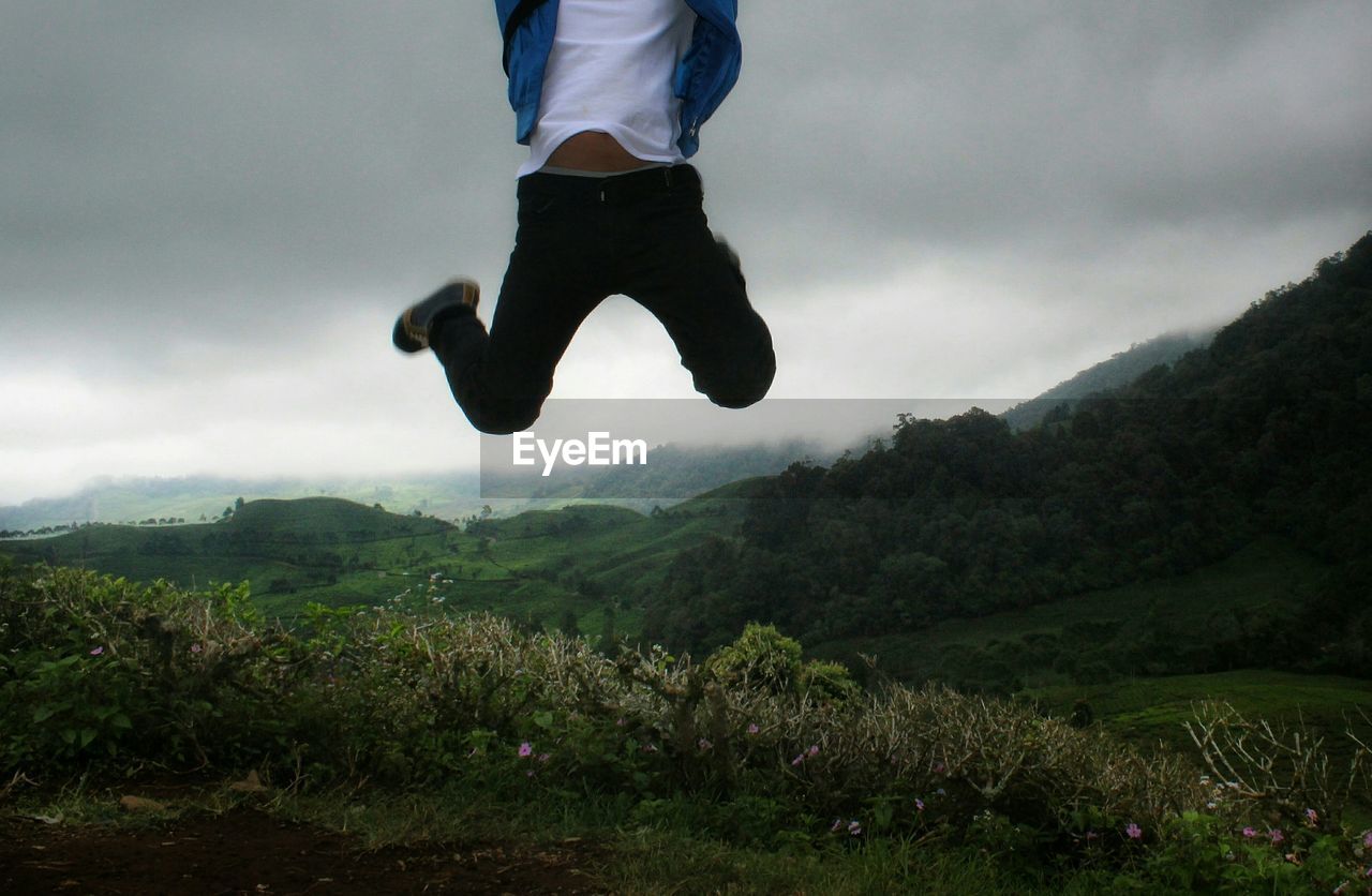 Low section of man jumping on mountain against sky