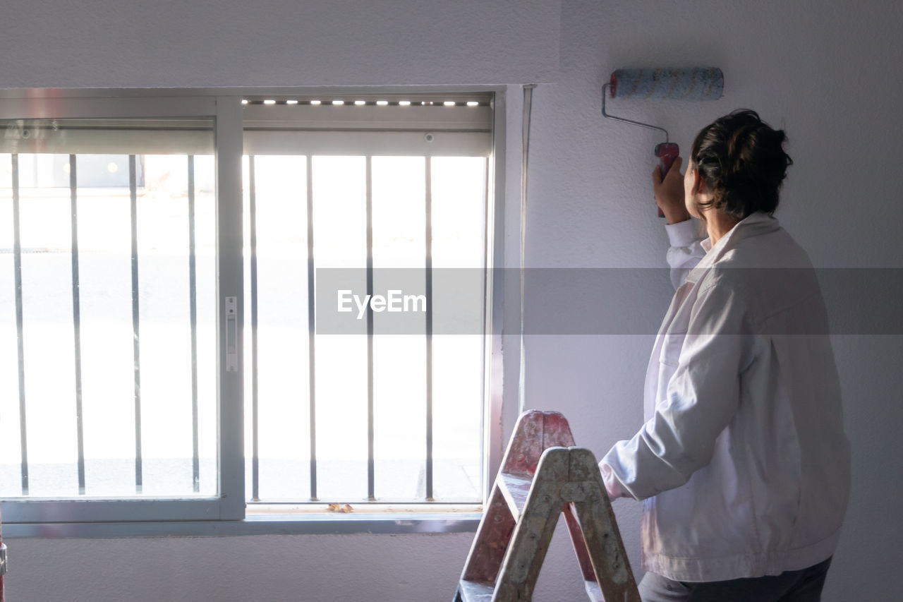 Young woman painting interior wall with white paint. paint cans and painter ladder.