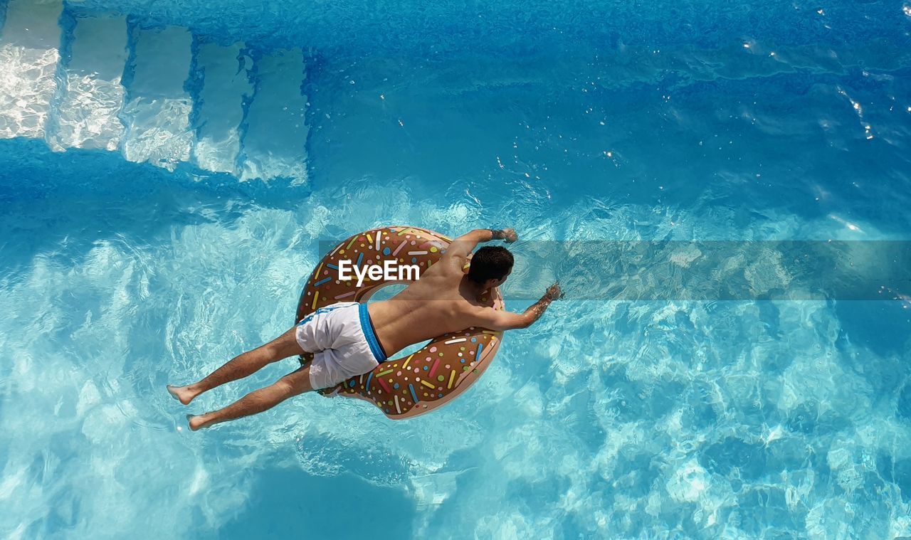 High angle view of man on donut inflatable ring in swimming pool