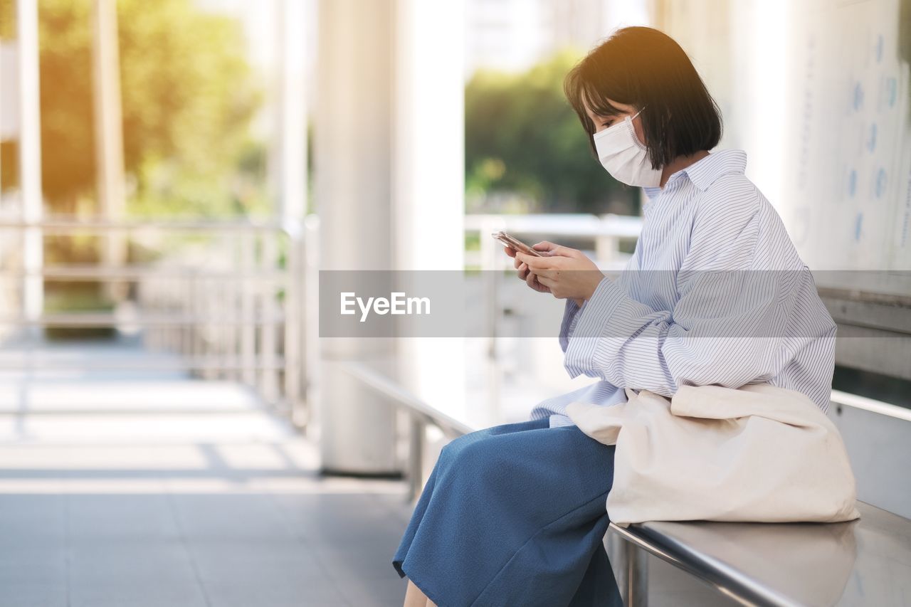 SIDE VIEW OF WOMAN USING PHONE WHILE SITTING ON MOBILE