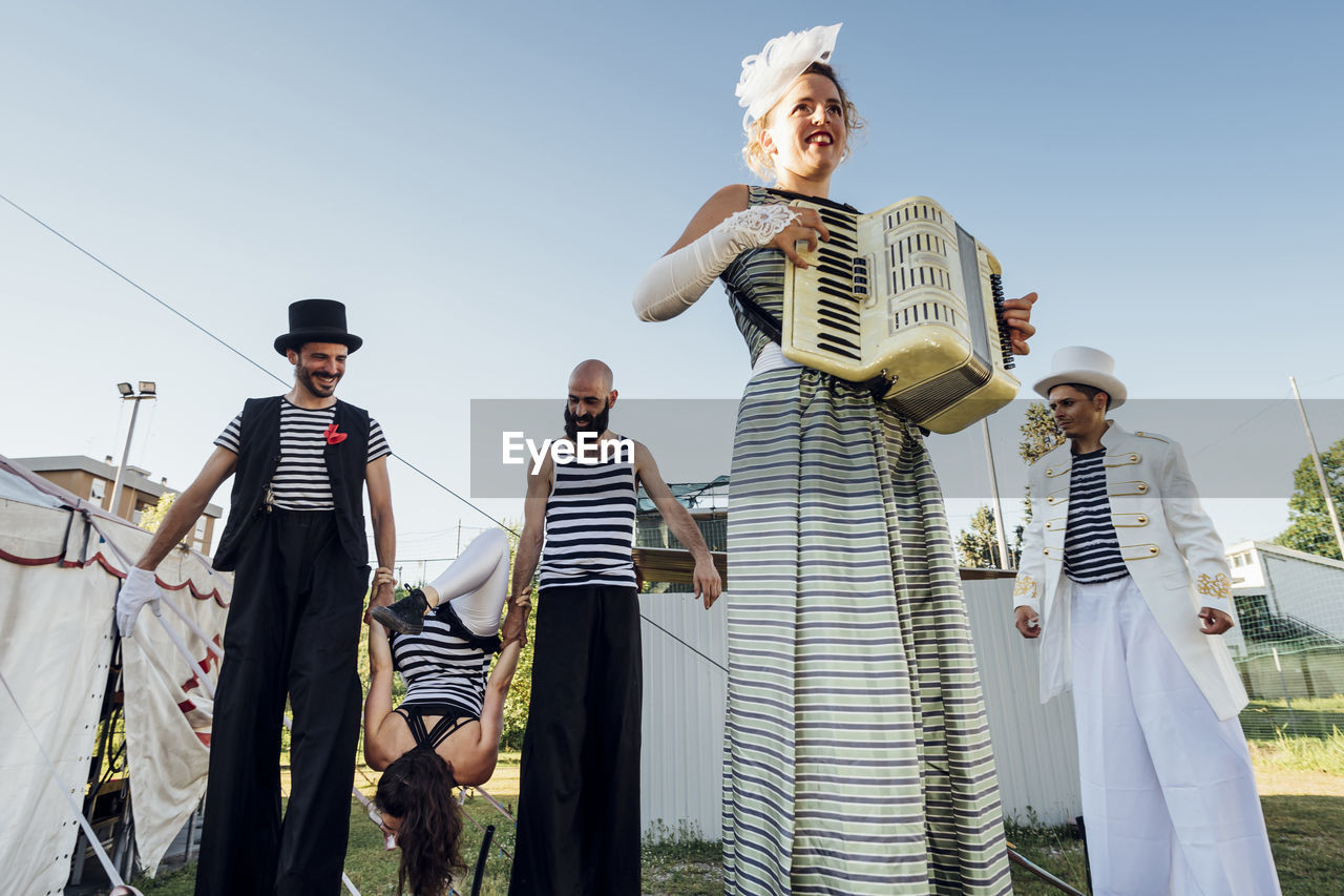 Female artist playing accordion while performers in background at circus