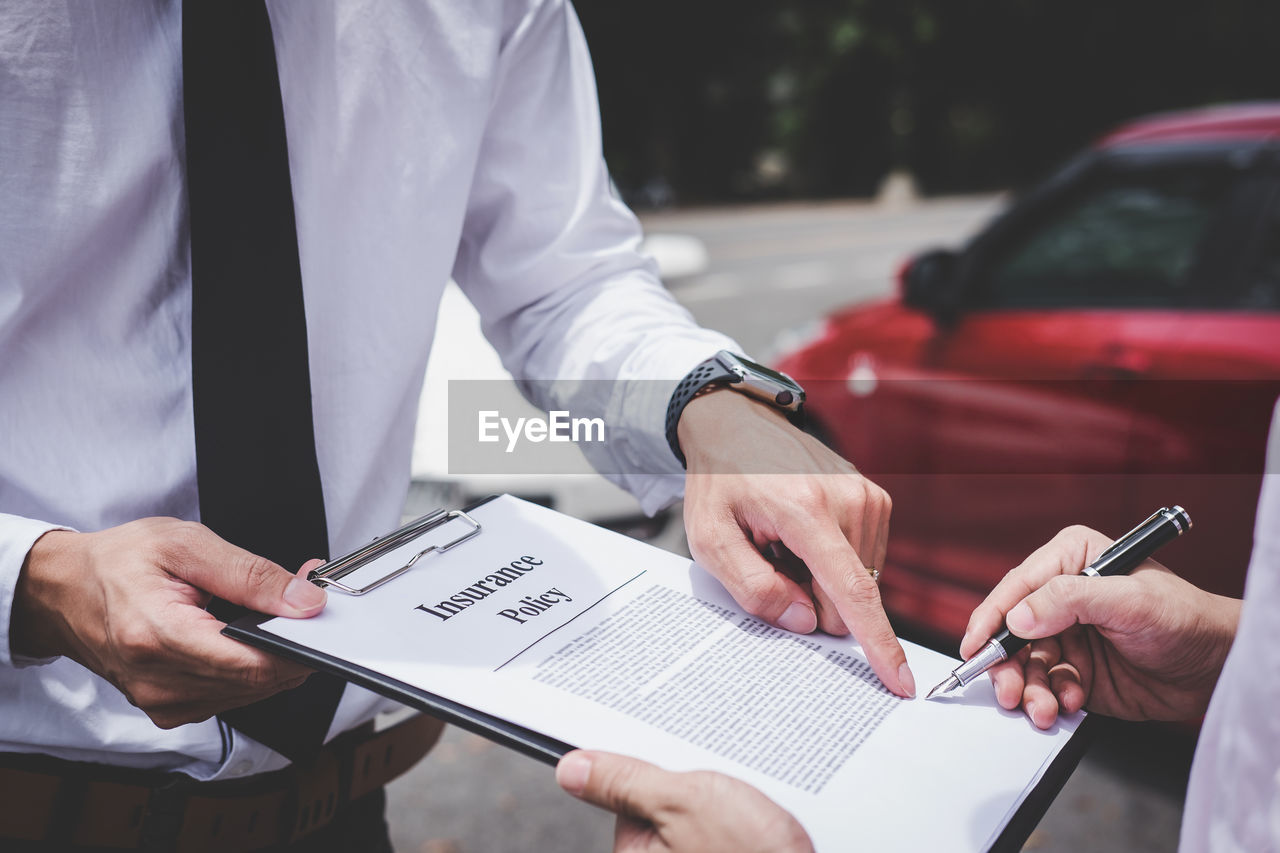 Midsection of customer signing contract while insurance agent holding clipboard