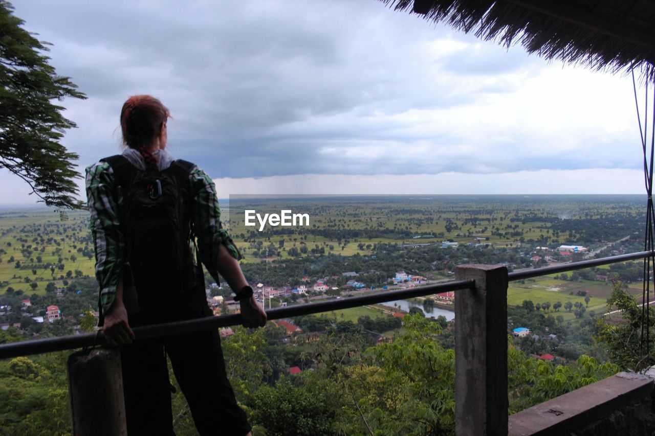 REAR VIEW OF MAN STANDING ON RAILING AGAINST CITYSCAPE