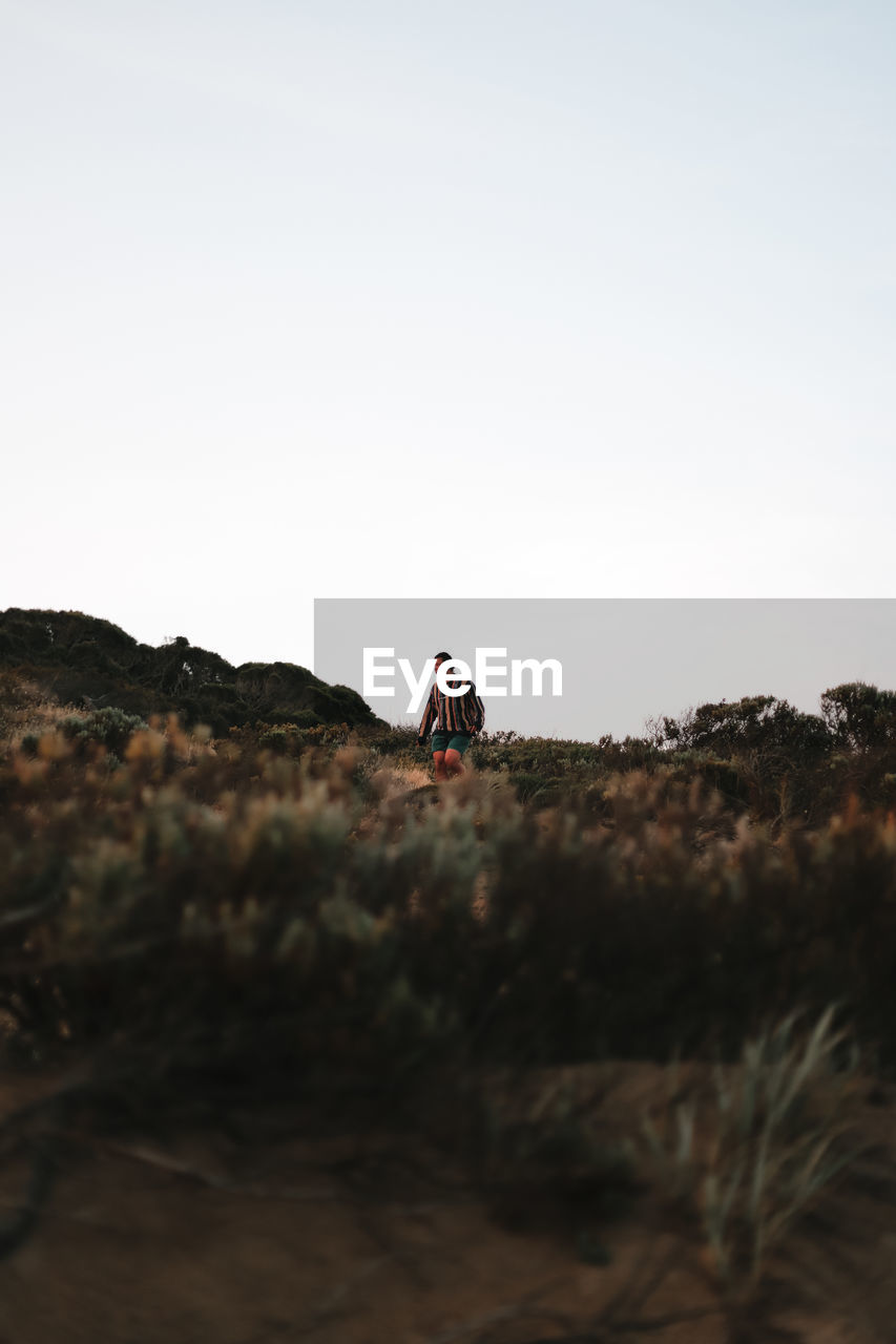 Distant view of man standing on land against clear sky during sunset