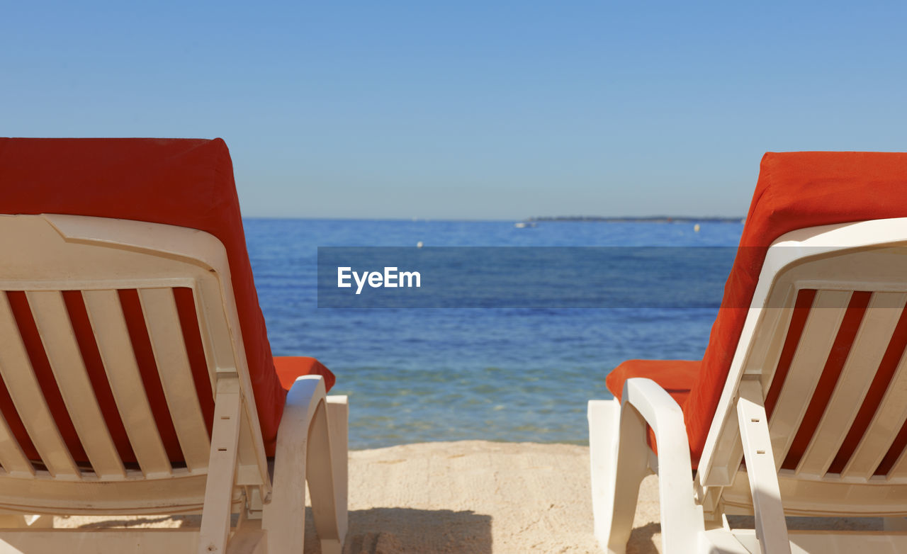 Scenic view of sea with chairs against clear blue sky