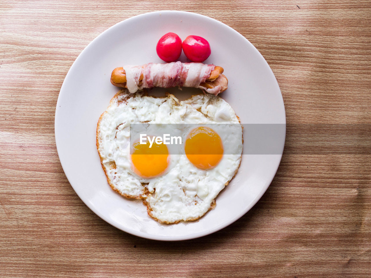 Breakfast skull fried eggs with tomato bacon and roll sausage in dish on wood table