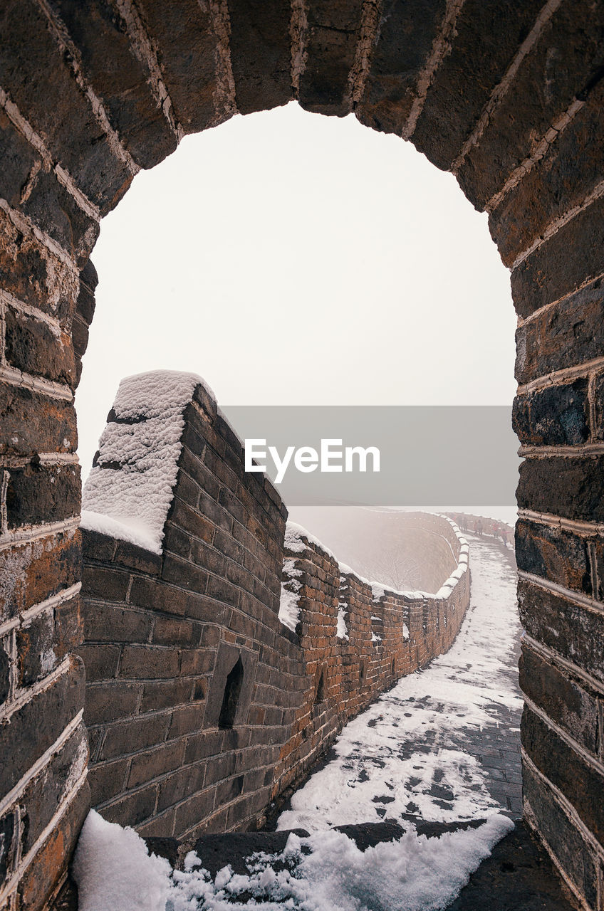 Arch leading towards walkway with snow against clear sky during winter