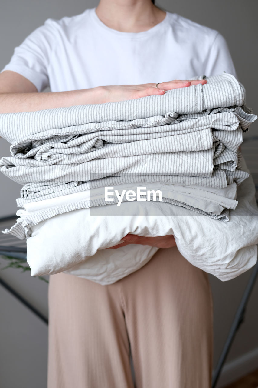 Stack of laundry and woman folding clean bedding and clothes