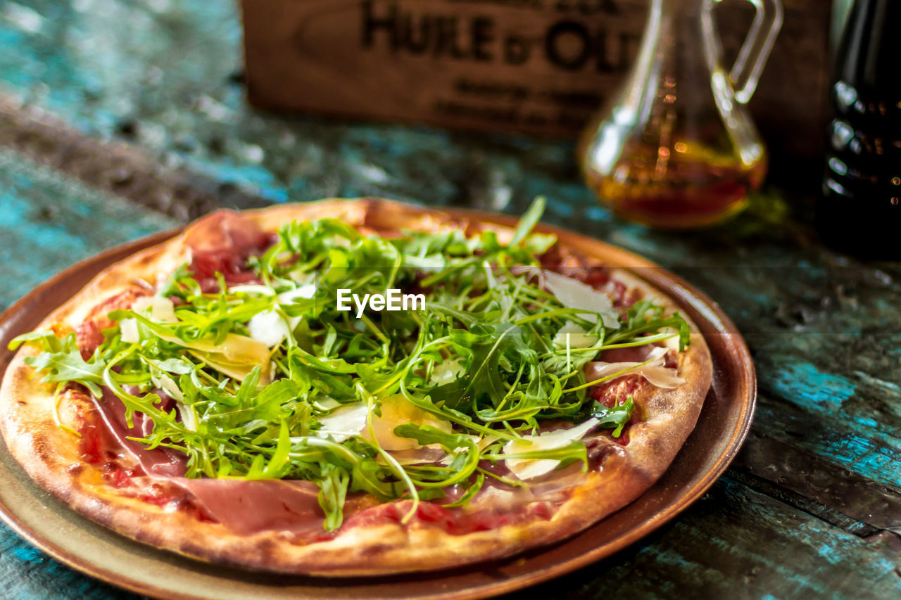 Close-up of pizza with arugula leaves in plate on table