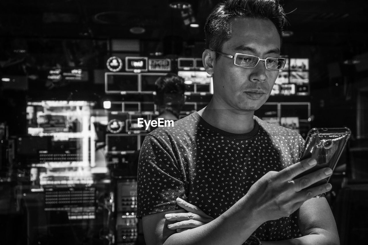 Mature man using mobile phone while standing against equipment in workshop