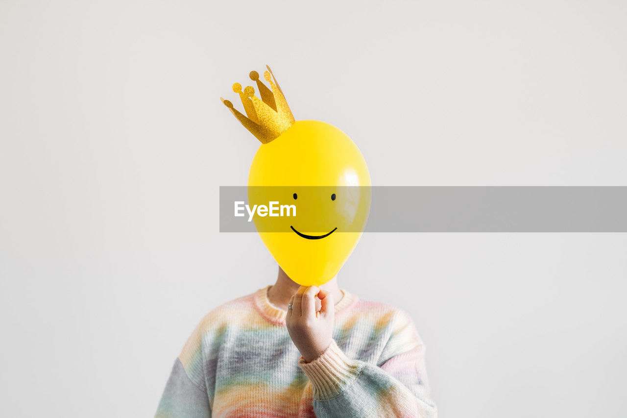 yellow, one person, smiley, studio shot, indoors, smiling, fun, humor, copy space, emoticon, adult, holding, happiness, anthropomorphic smiley face, front view, emotion, portrait, cartoon, obscured face, white background, toy, creativity, men, waist up, cheerful