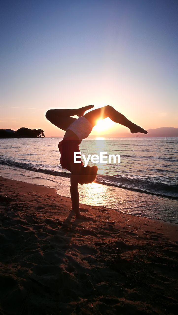 Silhouette woman doing handstand on beach against sky during sunset
