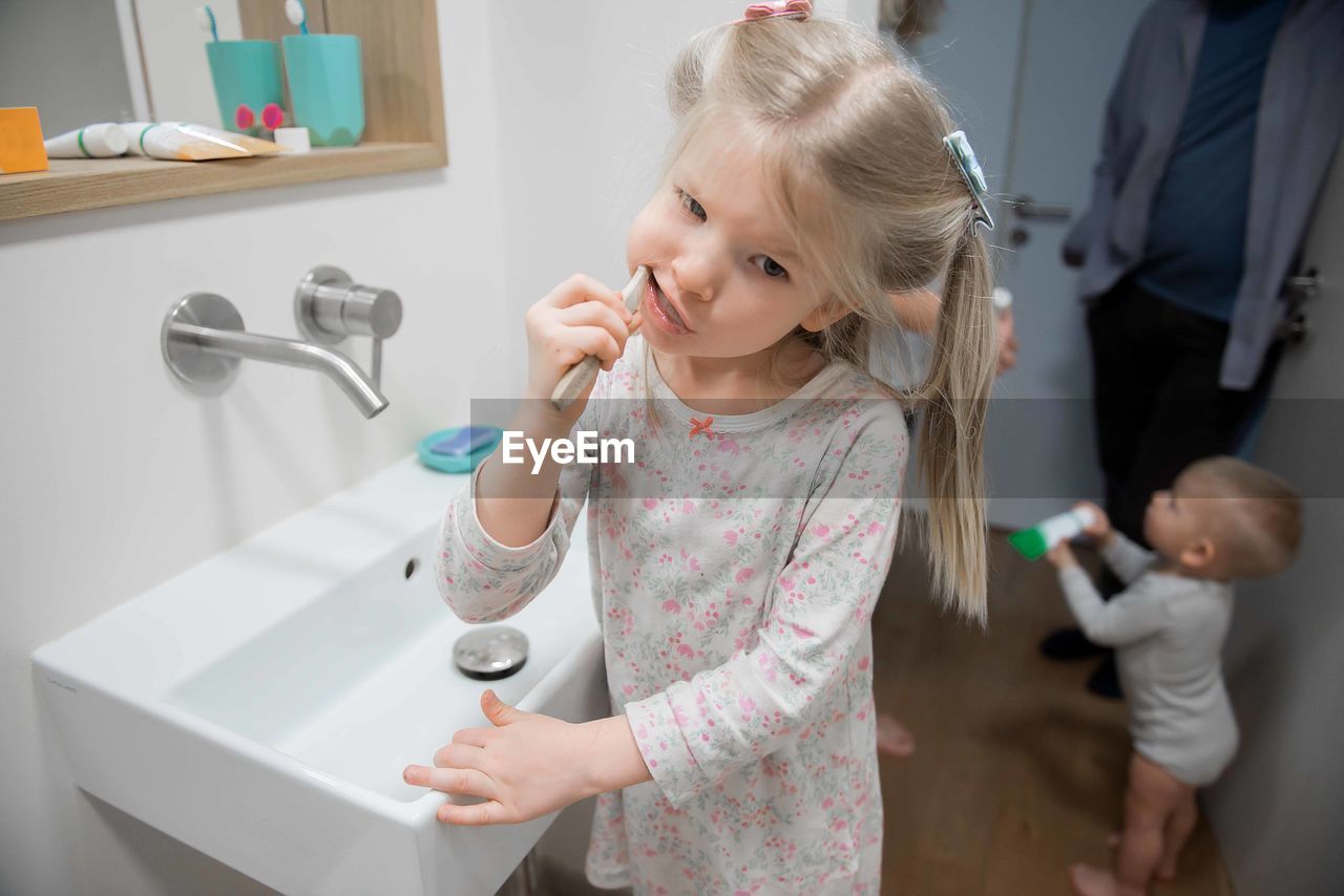 Girl brushing teeth by baby boy in bathroom at home