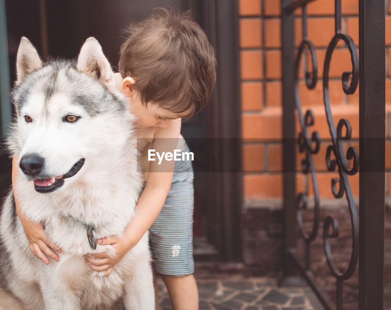 Shirtless boy holding with german shepherd on doorway