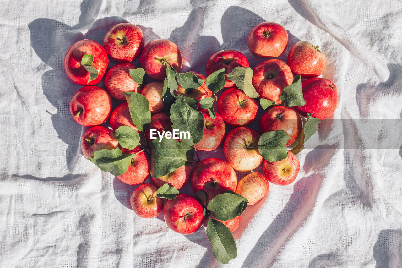 Autumn background of a small red apple and heart-shaped leaves on a beige linen textile background