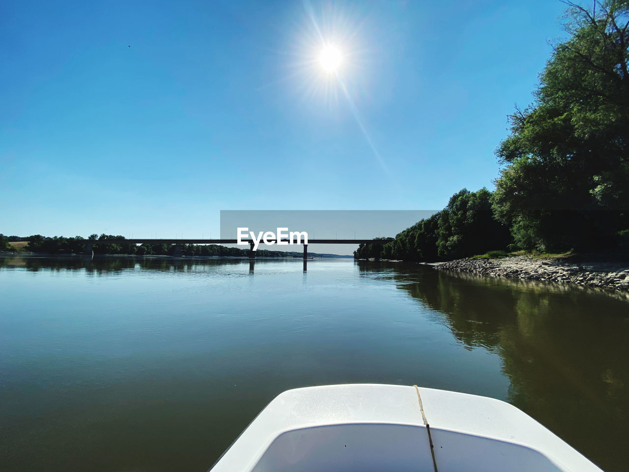 water, sky, reflection, nature, vehicle, beauty in nature, lake, sunlight, transportation, tranquility, scenics - nature, tree, blue, tranquil scene, boat, nautical vessel, no people, clear sky, sun, mode of transportation, day, travel, plant, sunny, outdoors, bay, travel destinations, environment, horizon, non-urban scene, idyllic, lens flare, land, summer, trip, vacation