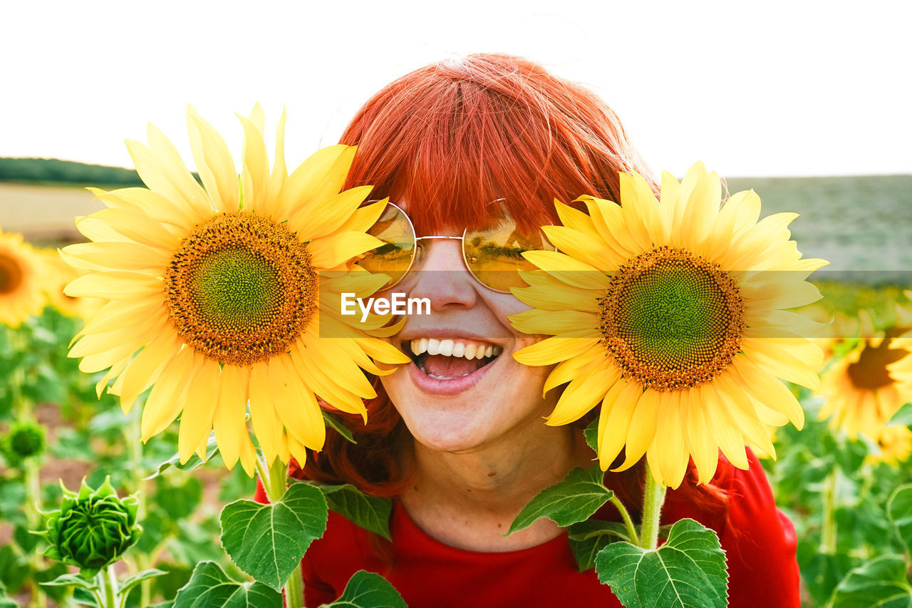CLOSE-UP PORTRAIT OF SMILING WOMAN AGAINST YELLOW SUNFLOWER