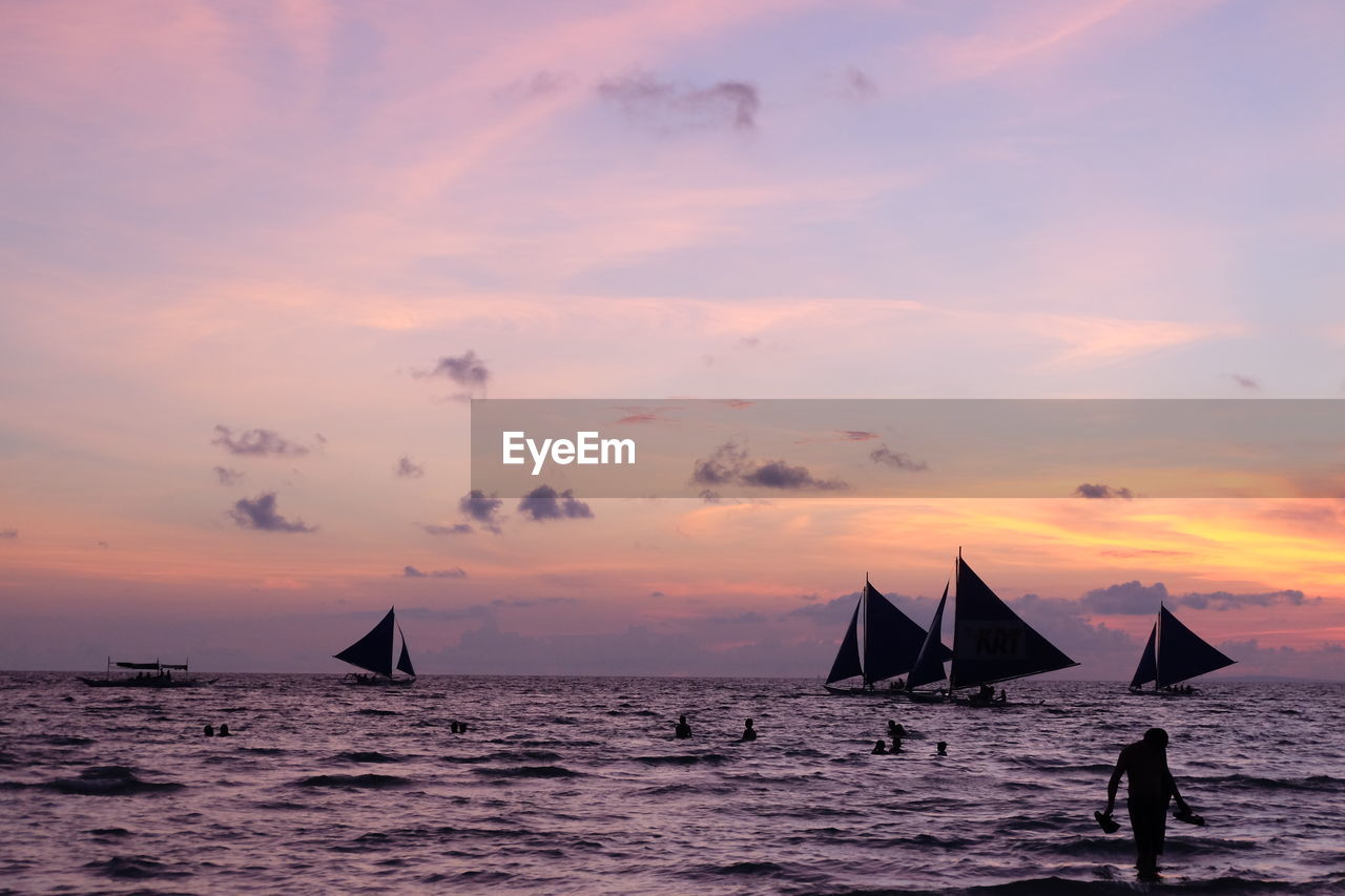 Sailboat sailing in sea at sunset with person in froreground