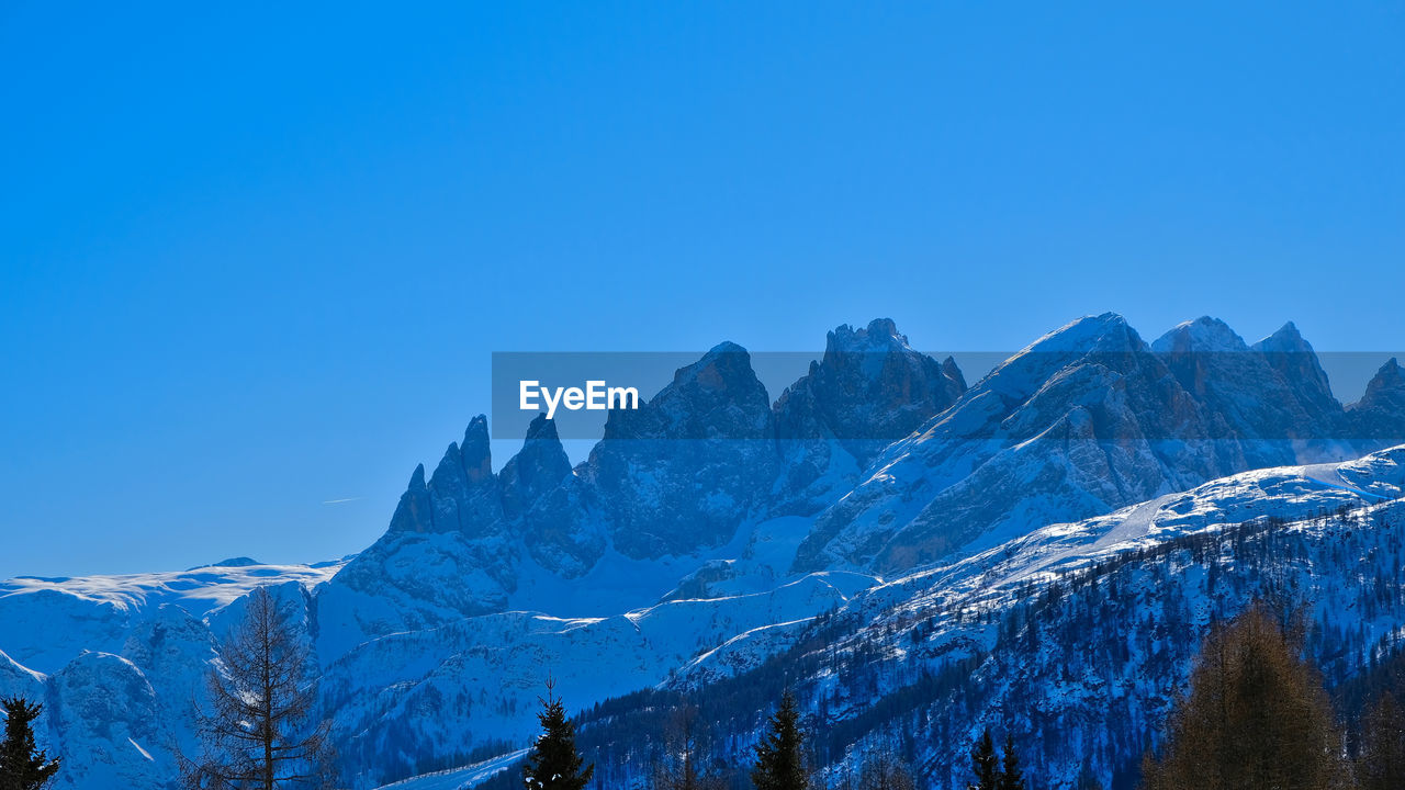 snow, mountain, winter, scenics - nature, cold temperature, sky, beauty in nature, mountain range, environment, landscape, snowcapped mountain, nature, blue, tree, travel destinations, forest, tranquil scene, land, clear sky, tranquility, plant, mountain peak, travel, no people, pine tree, coniferous tree, non-urban scene, ridge, outdoors, panoramic, pinaceae, tourism, pine woodland, idyllic, massif, leisure activity, day
