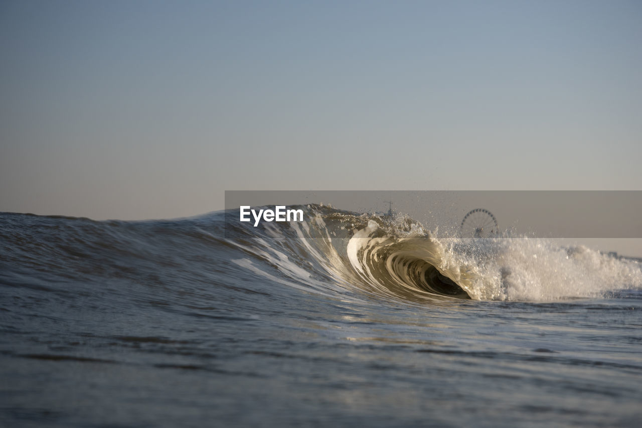 Waves splashing in sea against clear sky during sunset