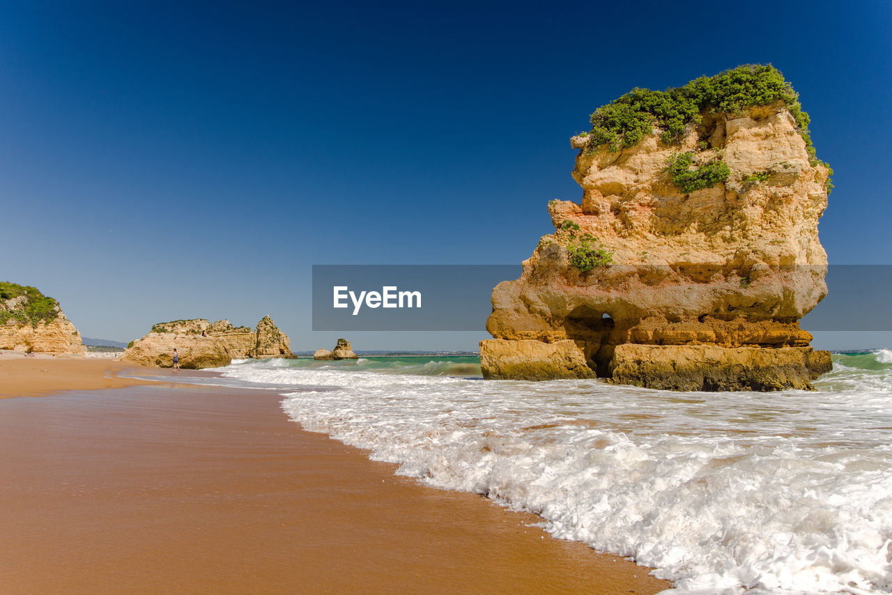 Rock formation on beach against clear blue sky