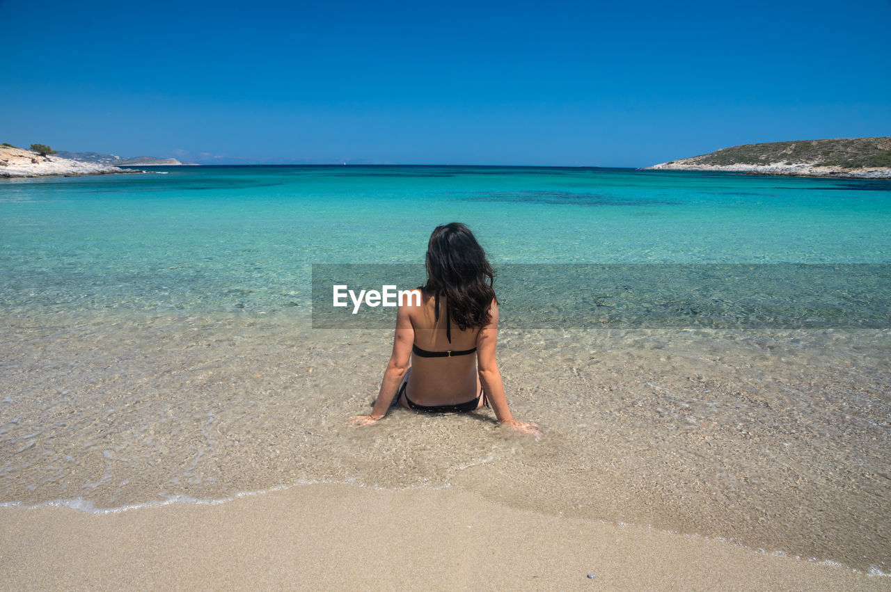 Rear view of woman wearing bikini sitting in sea