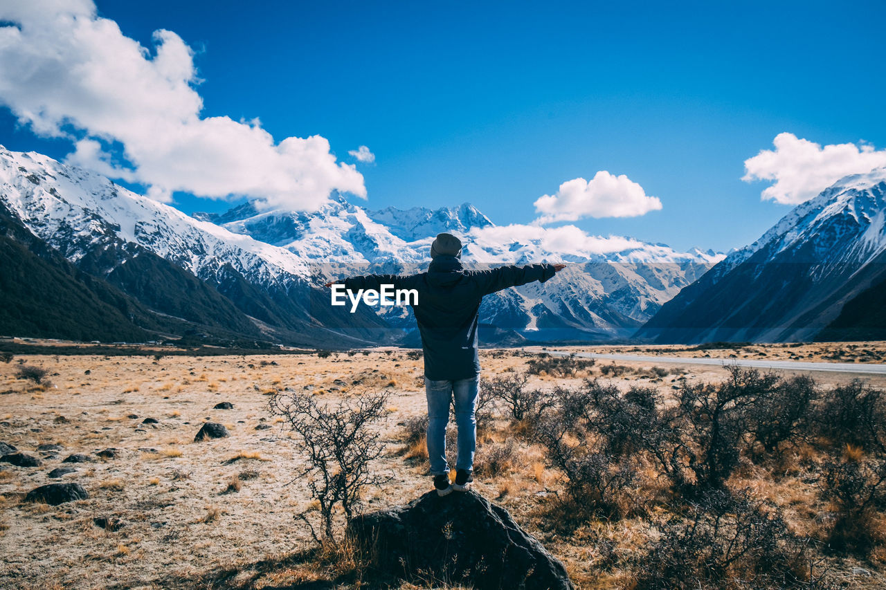 Man standing on field against snowcapped mountains